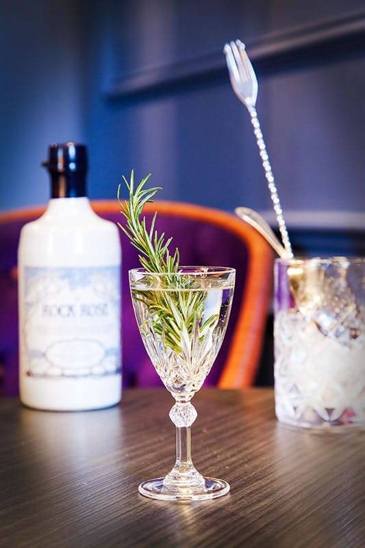 Bottle of Rock Rose Gin and Rock Rose Martini served in a vintage glass garnished with thyme sprig