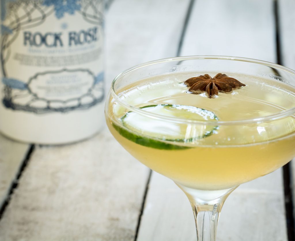 Bottle of Rock Rose Gin and house white cocktail served in a coupe glass and garnished with a slice of cucumber and star anise seed