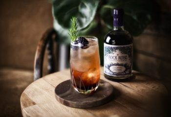 Bottle of Rock Rose Sloe Berries Gin and perfect serve in a large glass garnished with bramble and thyme sprig