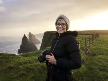 Portrait of Lisa Poulsen posing with her camera in front of the cliffs