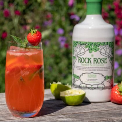 Bottle of Rock Rose Gin Summer Edition and Strawberry and Lime Gin Smash cocktail served in a tall glass and garnished with strawberry and mint leaf