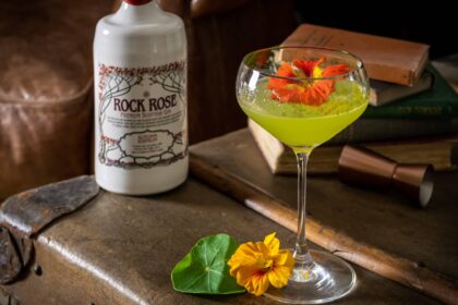 Bottle of Rock Rose Gin Autumn edition Green Thumb Cocktail served in a coupe glass and garnished with edible flowers