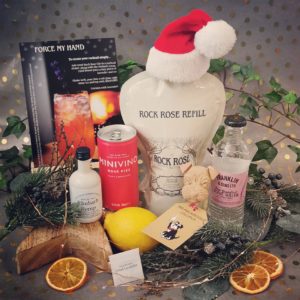 Content of the Refill Rewards Club box for December 2020 including Rock Rosie Gin pouch wearing a Santa's hat, can of rosé fizz, rhubarb syrup, lemonade and a Mr Mackintosh Lollipup