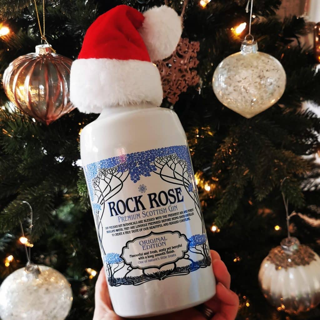 Bottle of Rock Rose Gin original edition wearing a Santa's hat in front of Christmas tree