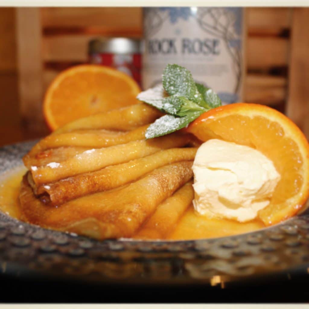Crepes Suzette on a plate with slices of orange, mint leaf and clotted cream