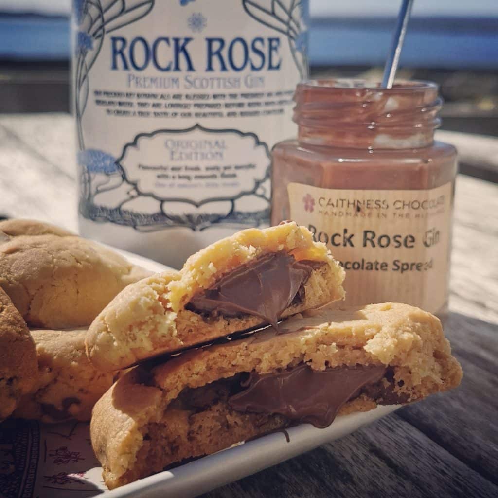 Rock Rose cookies filled with chocolate spread on a plate next to a bottle of Rock Rose Gin and a jar of Caithness Chocolate Rock Rose Gin chocolate spread