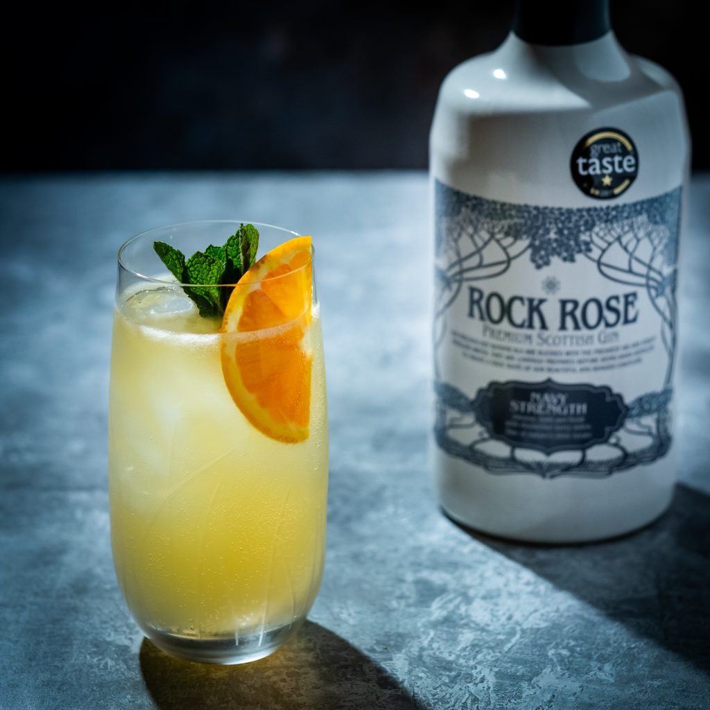 Bottle of Rock Rose Gin Navy Strength and Suffering Sailor cocktail served in a tall glass and garnished with a slice of orange and mint leaves