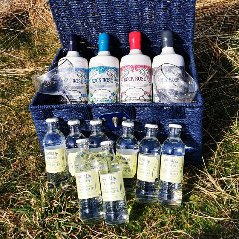 Content of the Rock Rose Gin Signature Collection Hamper including 4 bottles of Rock Rose Gin special edition, 8 tonic waters and 2 branded coupe glasses n a blue hamper