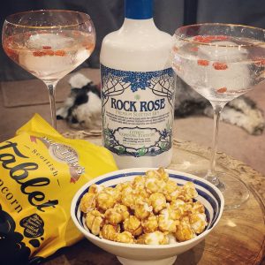 Bottle of Rock Rose Gin Citrus Coastal Edition, cocktail served in two branded coupe glass and tablet popcorn served in a ceramic bowl
