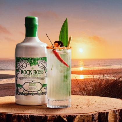 Bottle of Rock Rose Gin Summer Edition with Thai Gin Fizz cocktail served in a tall glass and garnished with desiccated coconut mixed with chilli powder to coat rim of glass and a whole fresh chilli (optional)