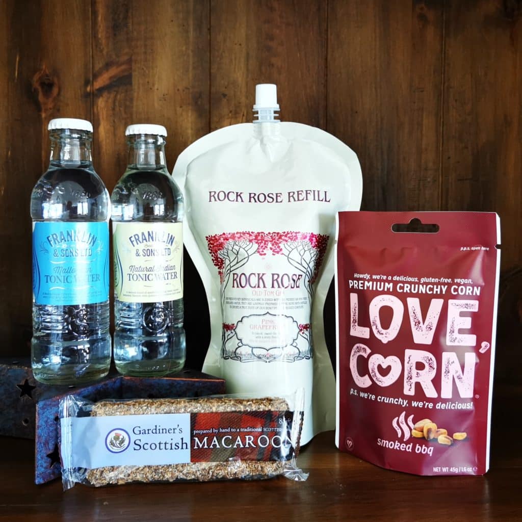 Content of the Refill Rewards Club box for August 2022 including Rock Rose Gin Pink Grapefruit pouch, tonic waters, Scottish Macarron, smoked barbecue corn