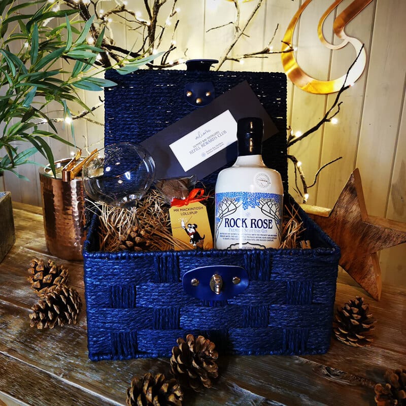 Content of the Refill Rewards Club Gift Set Hamper including a bottle of Rock Rose Gin, a branded glass, a Caithness Chocolate Mr Mackintosh Lollipup, a gift voucher for our Refill Rewards Club in a blue hamper