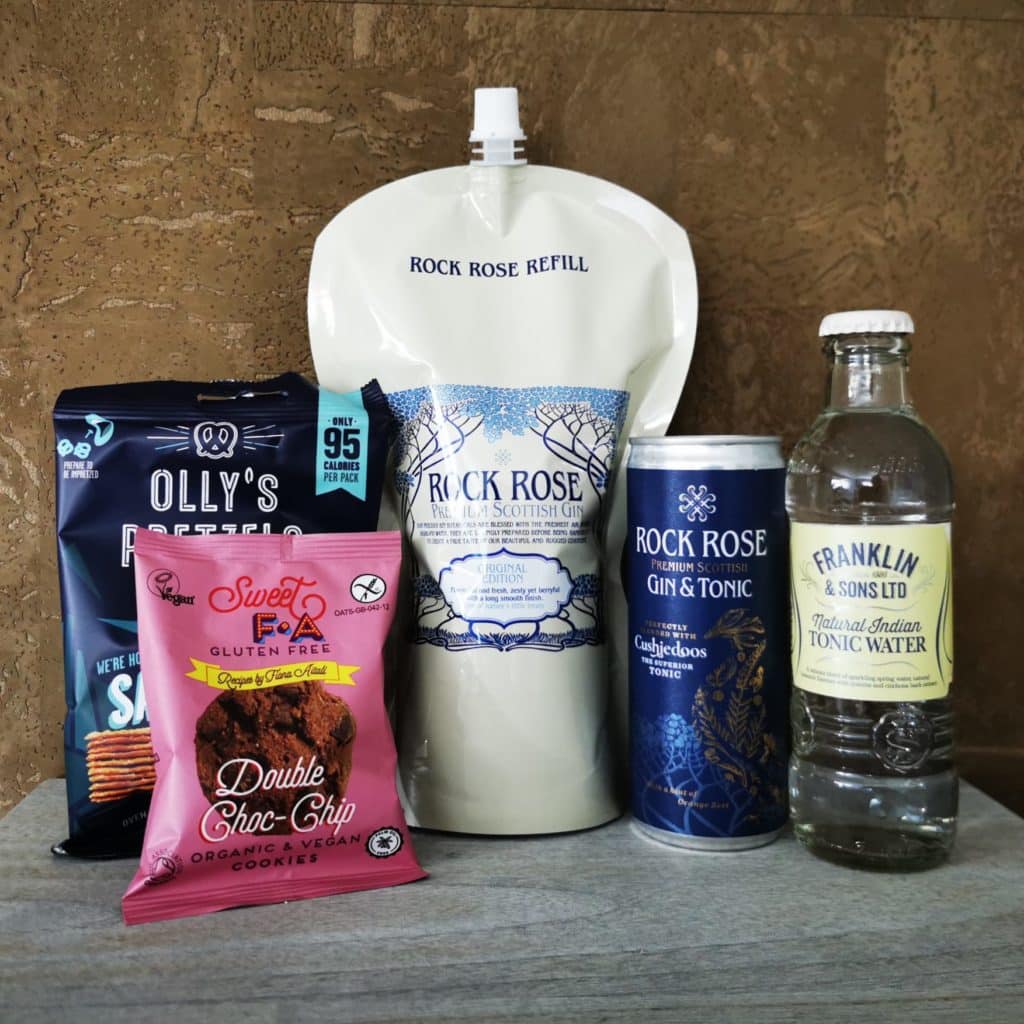 Content of the Refill Rewards Club box for October 2022 including Rock Rose Gin pouch, a Rock Rose Gin and tonic can, a tonic water, a pack of Olly's pretzel and organic and vegan cookies