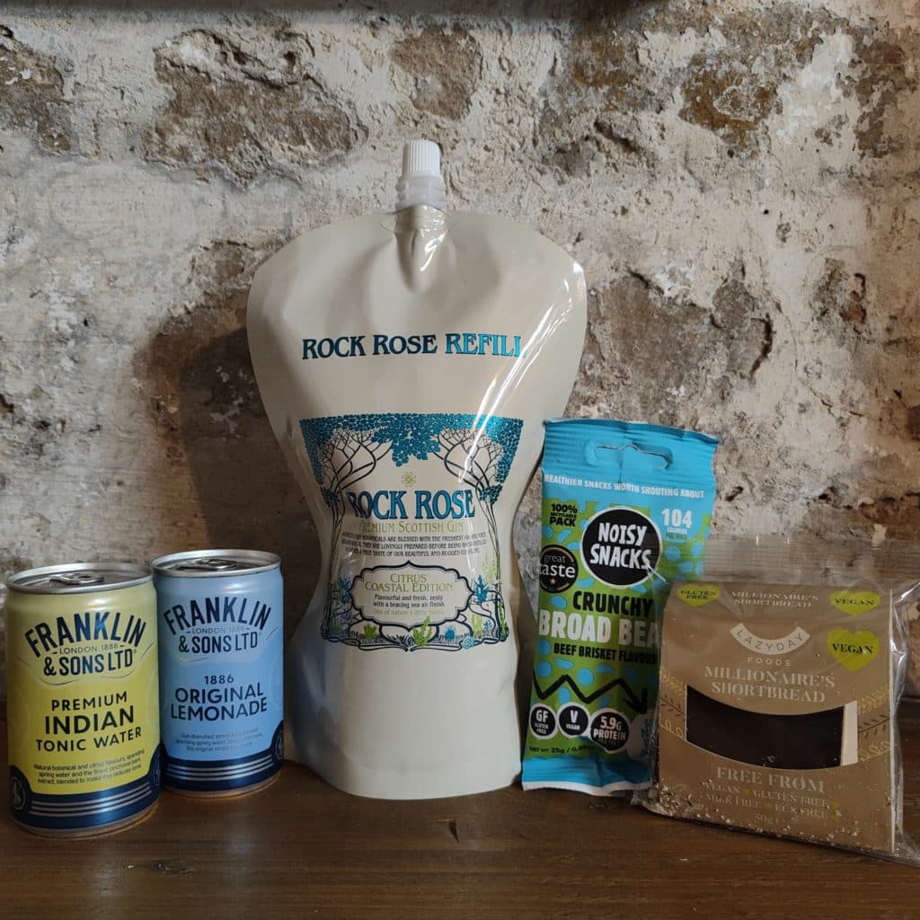 Content of the Refill Rewards Club box for March 2023 including Rock Rose Gin Citrus Coastal Edition pouch, 1 tonic water, 1 original lemonade, 1 crunchy broad beans snack and 1 pack of gluten free millionaire shortbread